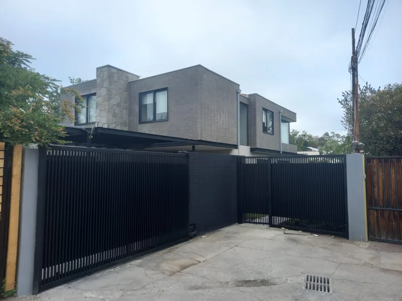 Fachada terminada de la casa reconstruida en Lo Barnechea, con portón corredizo y revestimiento oscuro