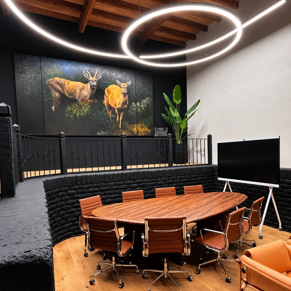 Salón terminado con mesa ovalada de reuniones, muro de ladrillo negro y línea de luz LED colgante